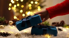 A hand places blue wrapped gifts on a festive background, surrounded by warm lights and holiday decor. Happy New Year and Merry Christmas. - Powered by Shutterstock - Get 15% off with code: PIKWIZARD15