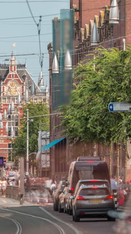 Damrak Street heading from Dam Square to Centraal Station in a timelapse with electric tram. Traffic moves on the road while people wait at the tram stop. Amsterdam, Netherlands