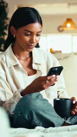 Coffee, phone and thinking with woman in home living room for internet or social media browsing. Drink, idea and typing with happy Indian person in apartment for communication or me time wellness