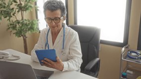 Senior doctor woman with grey hair working in a clinic office, using a tablet and laptop at her desk, showcasing a professional medical environment. - Powered by Shutterstock - Get 15% off with code: PIKWIZARD15