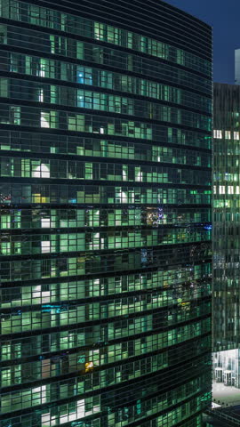 Aerial night timelapse of modern skyscrapers and towers in Brussels with glass facades and glowing windows. Illuminated urban skyline featuring Eglise Notre-Dame de Laeken in the background. Belgium