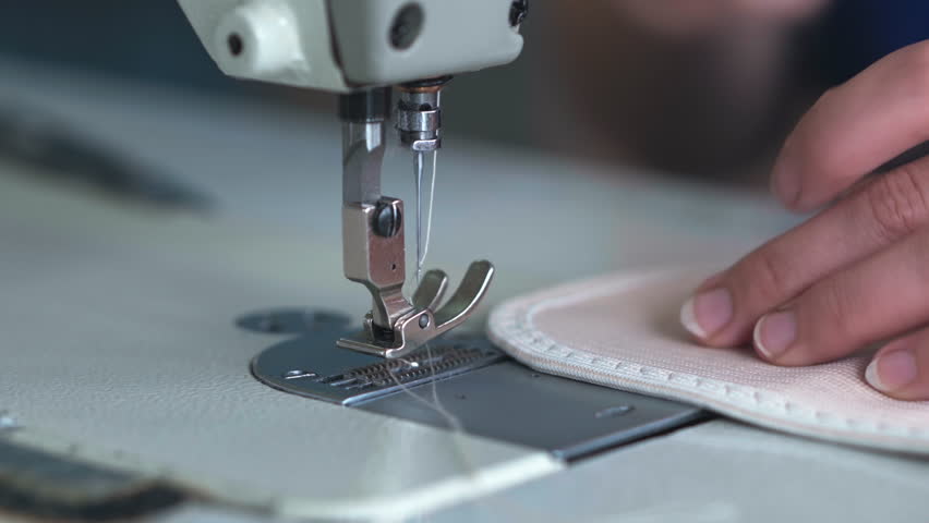 A close view shows hands guiding hook and loop compatible loop fabric under the needle of an industrial sewing machine, forming a clean seam with steady motion and precise control