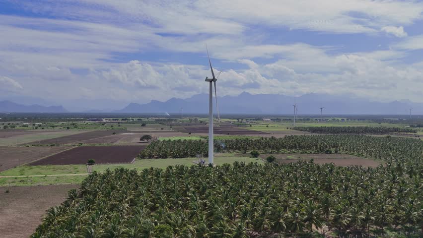 Tractor Plowing Green Field with Majestic Mountains and Spinning Wind Turbines in the Background on a Sunny Day. Farmers Working in Vibrant Green Rice Paddies, Showcasing Traditional India.