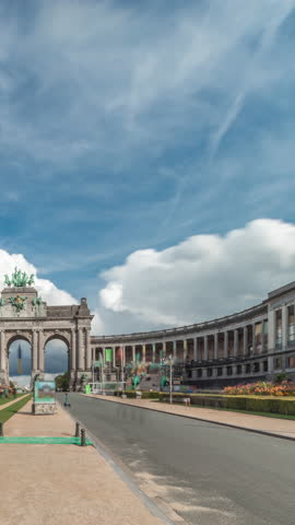 Hyperlapse of the Cinquantenaire Arcade in Jubelpark with flowerbed, Brussels, Belgium. The memorial triumphal arch stands tall under clouds timelapse, symbolizing Belgian history and independence.