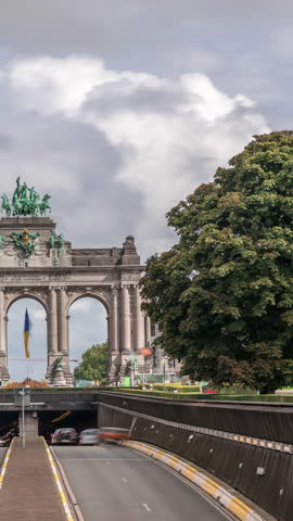 Timelapse of the Cinquantenaire Arcade in Jubelpark, Brussels, Belgium. The memorial triumphal arch stands tall under dramatic clouds, symbolizing Belgian history and independence. Traffic in a tunnel