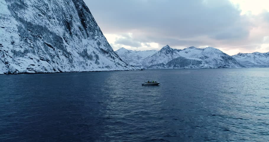Cinematic aerial drone footage of a small fishing boat on Arctic sea with dramatic snowy mountains and soft pastel sky near Senja in Northern Norway, perfect for travel and adventure content.
