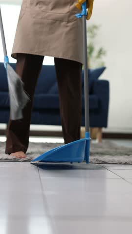Housekeeper sweeping dust into dustpan in living room.