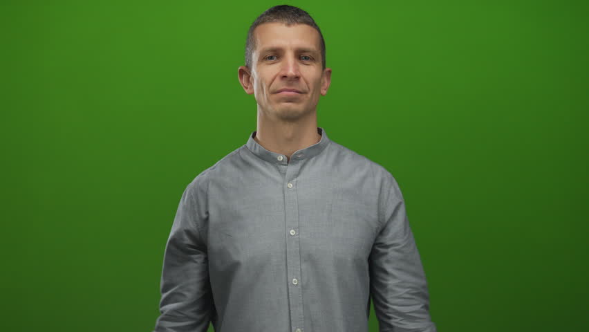 Confident man flexing muscles in front of green background showing strength and determination with a smile in casual gray shirt isolated indoors