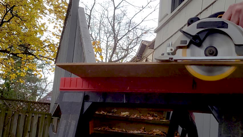 Outdoors carpenter using a battery powered circular saw ( no logos) to cut a sheet of wood, see the blade turning with sound