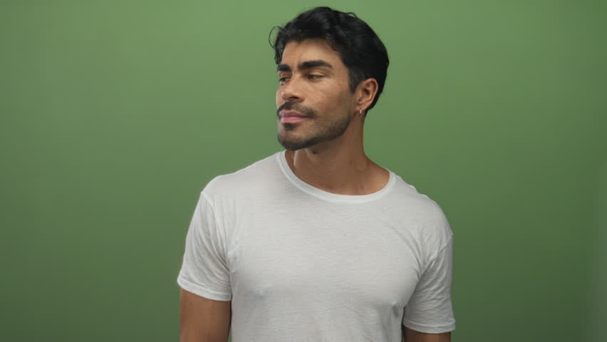 Young hispanic man wearing white t shirt with eyes closed and finger pointing to chest in green studio; confidence pride optimism assurance.