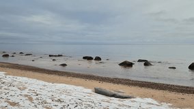 Calm winter shoreline with gentle waves, snow on the sand and scattered coastal rocks. Peaceful northern beach scene perfect for ambience, nature backgrounds and relaxation footage. - Powered by Shutterstock - Get 15% off with code: PIKWIZARD15