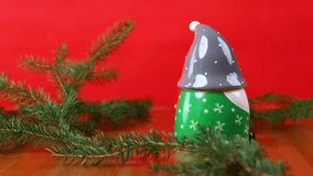 Two Christmas gnome candles rotating among spruce branches, red gnome with removed hat revealing candle wick - Powered by Shutterstock - Get 15% off with code: PIKWIZARD15