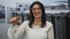 Woman makes rock horns gesture with her fingers while standing on a city street beside recycling bins; rock fun metal. - Powered by Shutterstock - Get 15% off with code: PIKWIZARD15