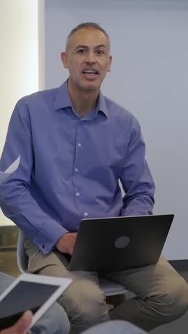 Vertical HD video of middle aged businessman leading a brainstorming session to gather project ideas. Confident leader guiding coworkers through creative discussion in a modern office