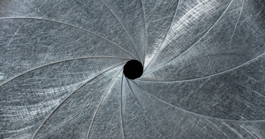 Circular blades of a mechanical iris create a precision opening controlling amount of light entering a camera lens with the opening mechanism controlling the aperture and the depth of field in focus.