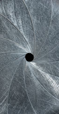 Circular blades of a mechanical iris create a precision opening controlling amount of light entering a camera lens with the opening mechanism controlling the aperture and the depth of field in focus.