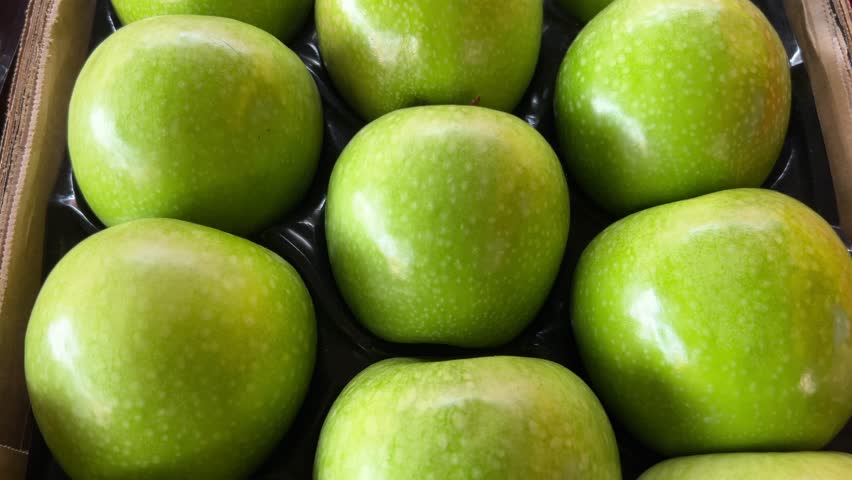Granny Smith variety apples arranged in crate, tracking shot on green apples