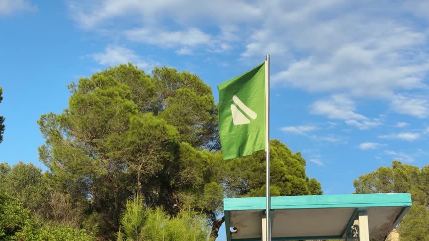 Green flag allowing to swim on top of lifeguard hut swaying in the wind on the beach of Spain close up
