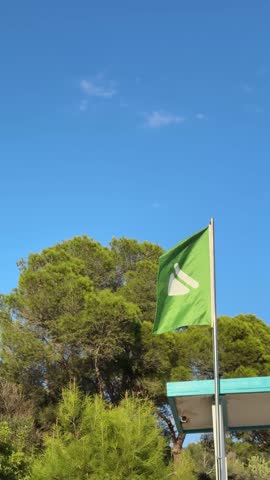Green flag allowing to swim on top of lifeguard hut swaying in the wind on the beach of Spain close up
