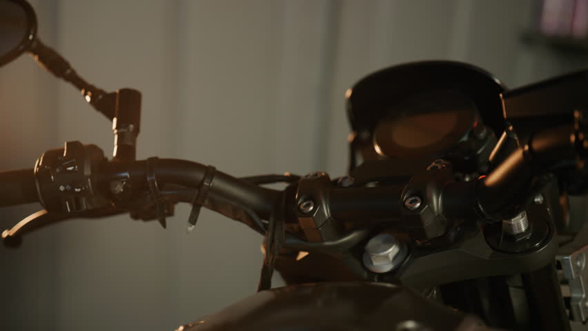 Close-up view of motorcycle handlebar showing controls and mirror in a dimly lit garage setting during evening hours