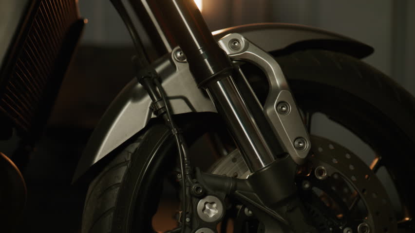Close-up view of a motorcycle front fork showcasing suspension details in a dimly lit garage setting at night