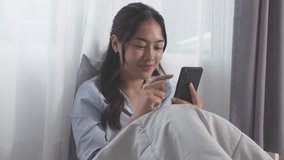 Asian Young woman smiling while using smartphone bed natural light cozy bedroom scene relaxed mood casual outfit indoor lifestyle. young woman using smartphone bed with soft natural light and blanket - Powered by Shutterstock - Get 15% off with code: PIKWIZARD15