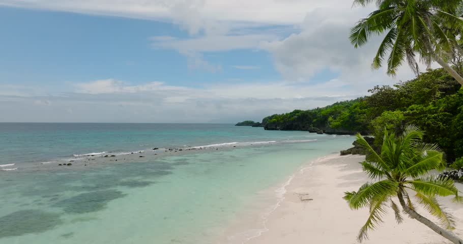 Clear turquoise sea water and waves on white sandy beach with coconut trees. Carabao Island, Romblon. Philippines.