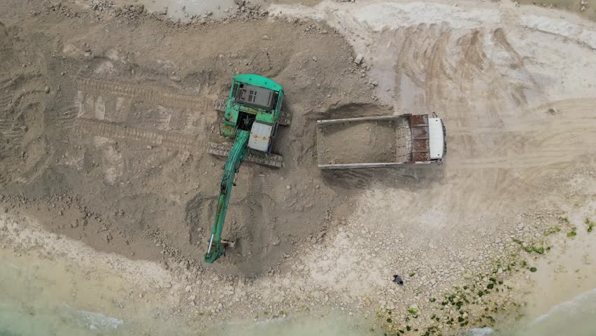 Aerial tracked excavator reshaping sandy coastline, green tracked machine digs and pushes sand to form