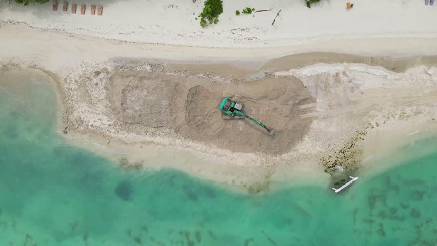 Aerial tracked excavator reshaping sandy coastline, green tracked machine digs and pushes sand to form