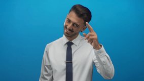 Man in white shirt and navy tie smiling and pointing finger at camera in studio with blue wall; confidence. - Powered by Shutterstock - Get 15% off with code: PIKWIZARD15