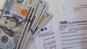 Top view of US dollar bills, tax forms, a pen, and a calculator, highlighting personal finance, tax preparation, accounting, and money management tasks. - Powered by Shutterstock - Get 15% off with code: PIKWIZARD15