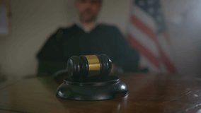 Close-up of a judge’s hand holding a wooden gavel with the American flag in the background, symbolizing law, justice, and the U.S. judicial system in a courtroom setting. - Powered by Shutterstock - Get 15% off with code: PIKWIZARD15