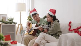 Happy young couple enjoying Christmas holiday at home, family people relax on cozy couch celebrating xmas with festive tree and presents, man plays guitar for woman smiling listening. - Powered by Shutterstock - Get 15% off with code: PIKWIZARD15