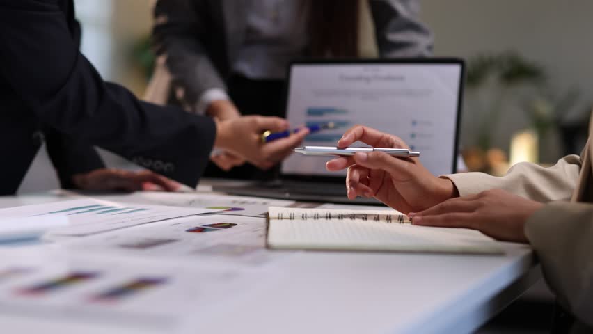 Asian businesswoman analyzing financial charts and graphs, discussing strategies and pointing at important data during meeting.