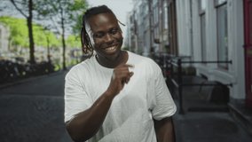 Man young with dreadlocks wearing white t shirt finger to lips for silence on city street lined with bicycles and townhouses; secrecy hush. - Powered by Shutterstock - Get 15% off with code: PIKWIZARD15