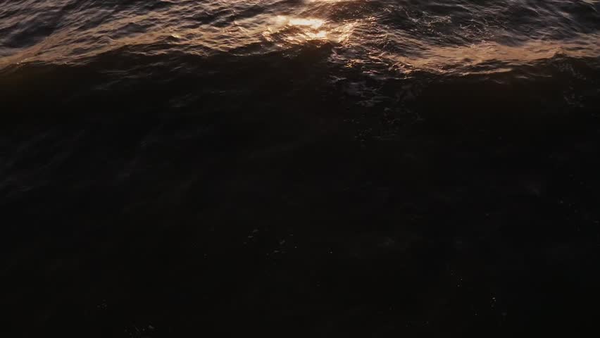 Golden sunlight reflects off dark sea waters in a top-down drone view, capturing shimmering waves and dynamic patterns in a serene ocean scene.