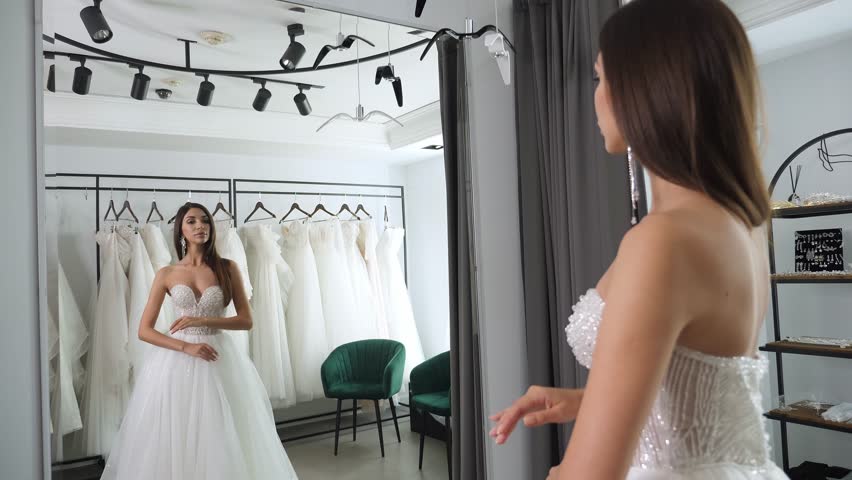 Portrait of a gorgeous woman with long hair in a beautiful wedding dress in front of a mirror in a wedding salon. A bride in a wedding dress, in a boudoir for a wedding.