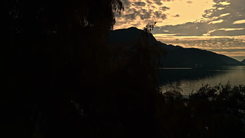 Lugano, Switzerland – December 3, 2024: Evening view from Parco Ciani toward Lake Lugano, Campione d’Italia and the surrounding mountains at dusk with a tour ship in the distance.