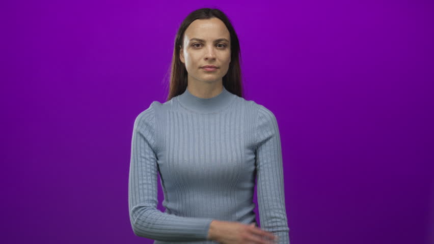 Young woman in ribbed sweater points finger upward in studio against purple wall while crossing her arm; curiosity.