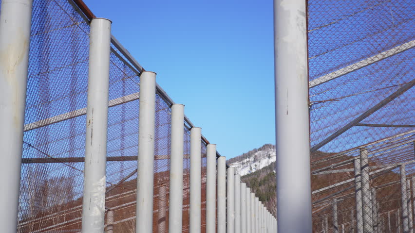 Harsh metal structure built from rigid beams and mesh rises above white frozen hillside. View creates mixed winter mood with bold geometry