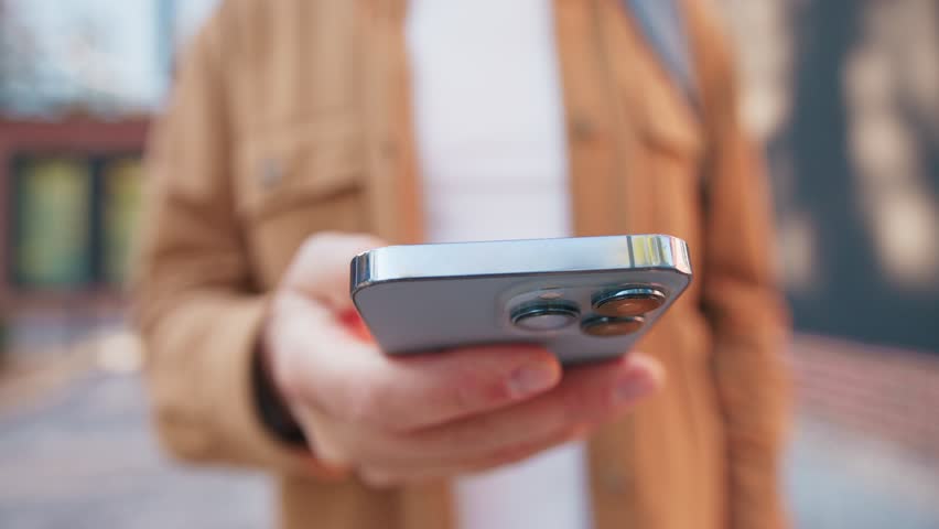 Close camera view person holding smartphone and entering information by tapping on touch screen. Focus on top edge of device while user standing outside. Detailed shot capturing simple interaction.