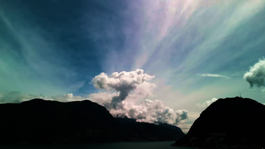 Lugano, Switzerland – August 18, 2024: Dramatic cloud formations tower above Lake Lugano, Monte San Salvatore, and Monte Caprino, with billowing cumulus rising into streaked high-altitude clouds.