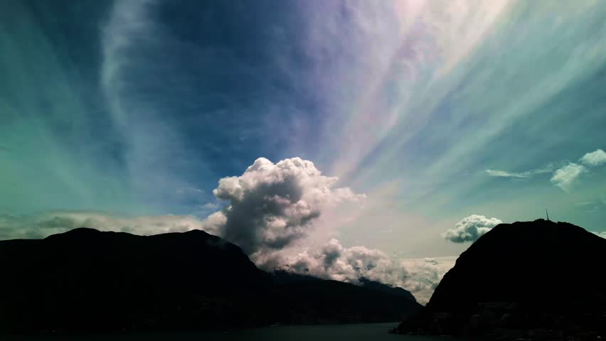 Lugano, Switzerland – August 18, 2024: Dramatic cloud formations tower above Lake Lugano, Monte San Salvatore, and Monte Caprino, with billowing cumulus rising into streaked high-altitude clouds.