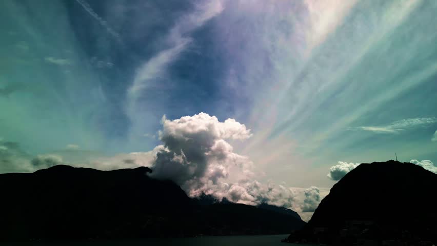 Lugano, Switzerland – August 18, 2024: Dramatic cloud formations tower above Lake Lugano, Monte San Salvatore, and Monte Caprino, with billowing cumulus rising into streaked high-altitude clouds.