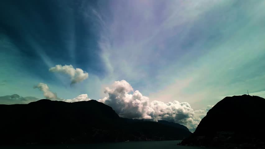 Lugano, Switzerland – August 18, 2024: Dramatic cloud formations tower above Lake Lugano, Monte San Salvatore, and Monte Caprino, with billowing cumulus rising into streaked high-altitude clouds.