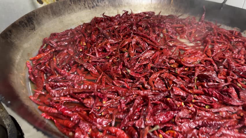 Boiling dried red chilies in a large cooking pan during food preparation process in a kitchen.