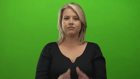 Young blonde woman wearing black top frowning with clasped hands praying in green studio set; faith devotion. - Powered by Shutterstock - Get 15% off with code: PIKWIZARD15
