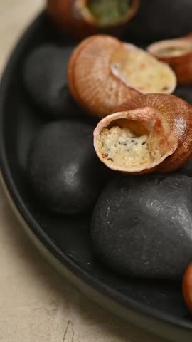 French stuffed snails in shells served on black stones. Close-up food video showing the dish on a plate and a fork taking one snail.