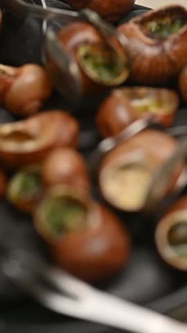 French stuffed snails in shells served on black stones. Close-up food video showing the dish on a plate and a fork taking one snail.