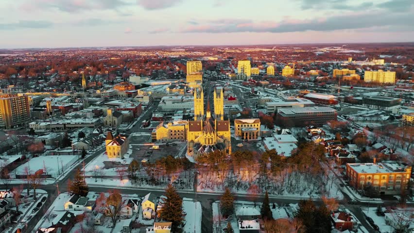 A drone view looking northeast, pushing in over the glowing buildings of East Portland at dusk. Soft twilight colors highlight the urban skyline, streets, and illuminated architecture as night approac